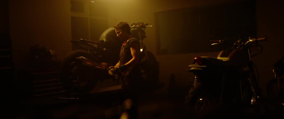 A young woman walks in to her garage and picks up tools to work on her motorcycle