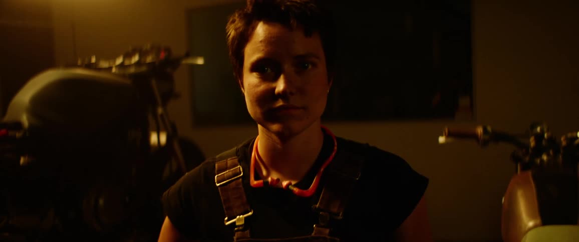 A woman standing in a garage between two motorcycles
