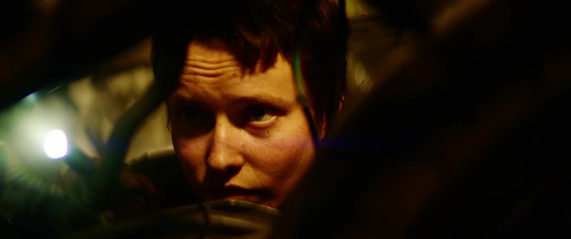 A woman with short hair holds a flashlight and carefully inspects her project