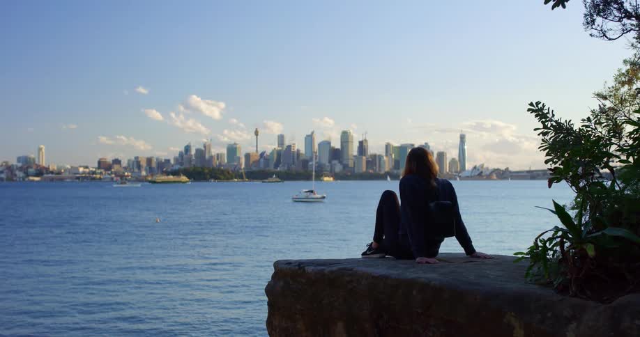 A woman sitting outside looking at a city across a lake