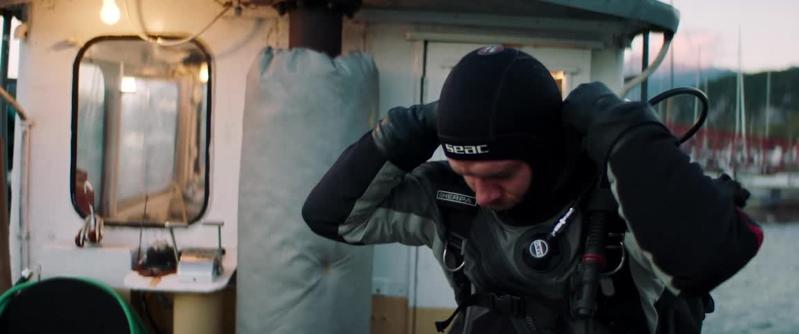 Man puts on scuba gear on boat in harbor