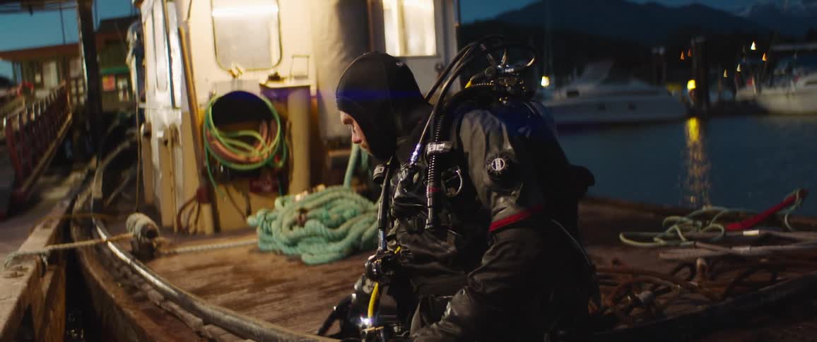 A diver resting on the deck of a small boat begins to remove his diving equipment