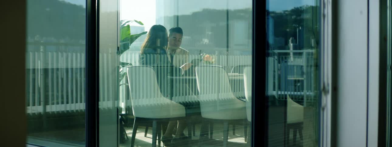 A man and woman sit at a table in an office and speak while looking at a tablet