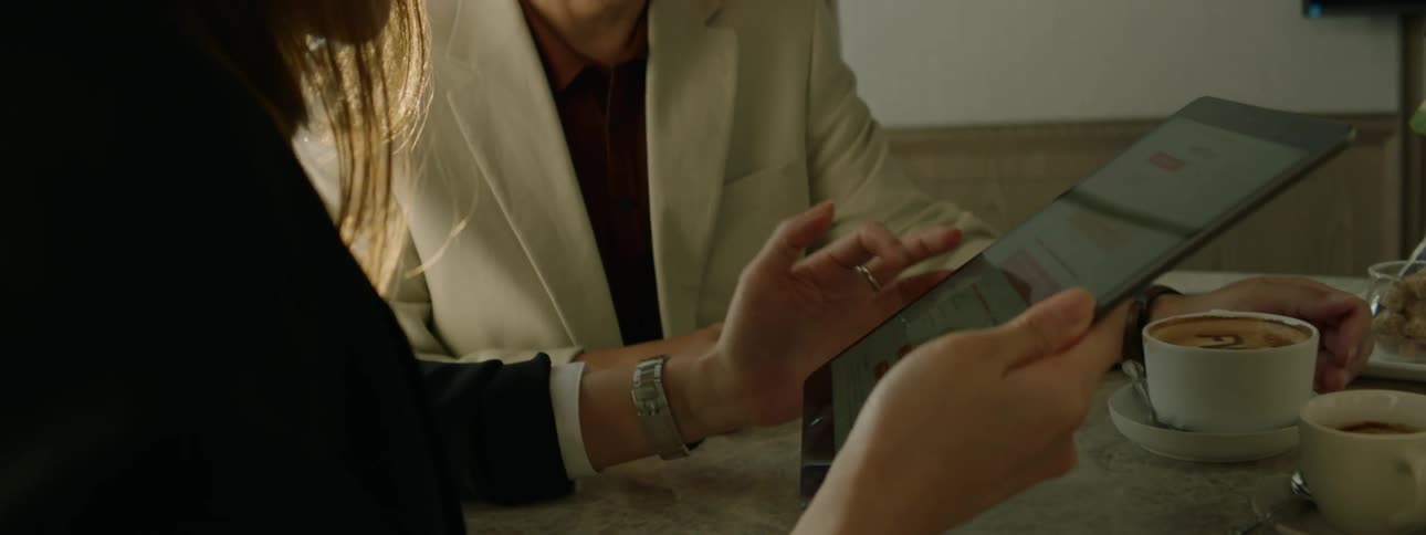Two people sit at an office table together looking over a tablet