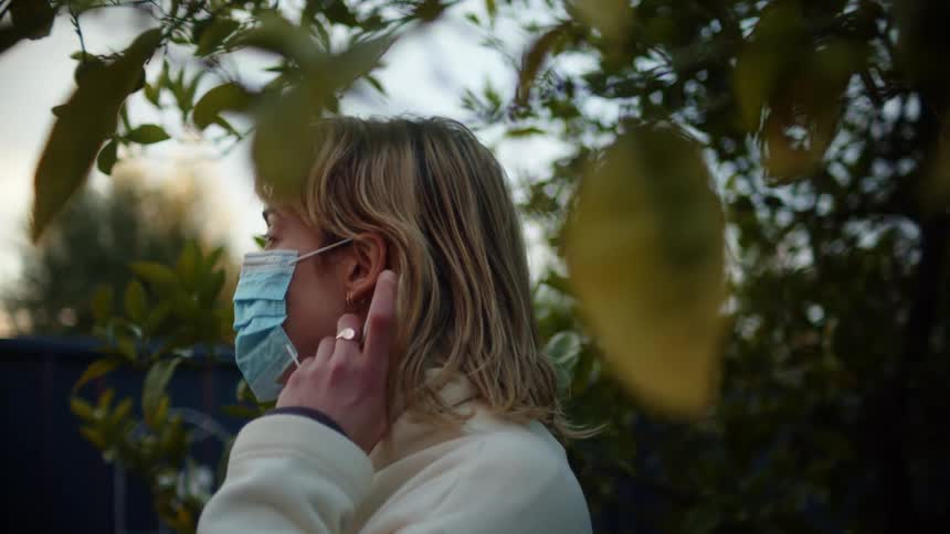 A woman puts on mask outdoors at dusk