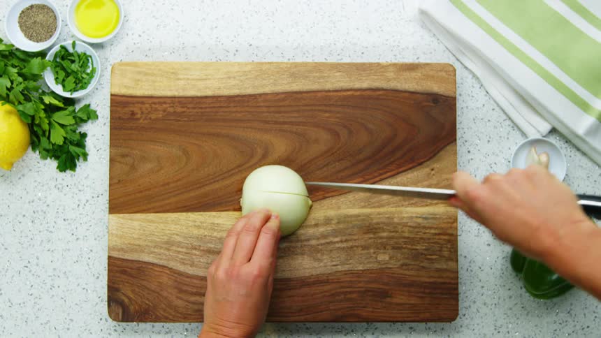 A person slicing a yellow onion on a wood cutting board with a knife