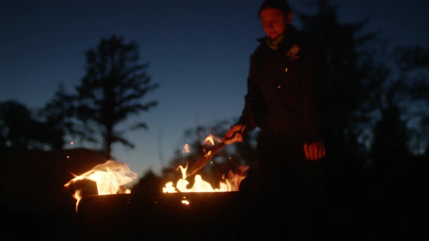 A person holding a stick over a fire outside in the dark