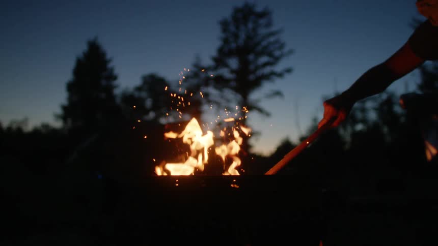 A person lighting a piece of wood from acamp fire in the woods