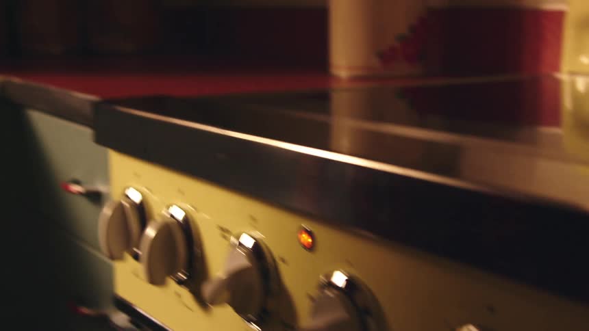 An elderly woman in a kitchen places a tray of cookies in the oven before removing her oven mitt