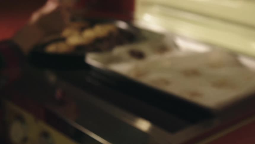 An elderly woman takes cookies off of a cookie sheet and puts them on a tray and carries them to a table in her home