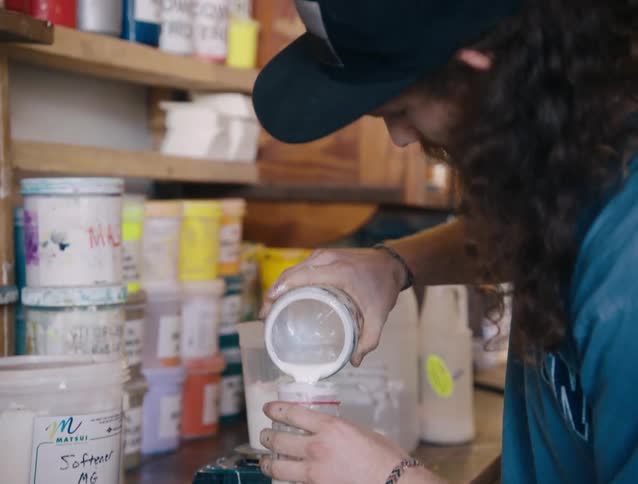 A male store employee pours paint from one jar to another jar