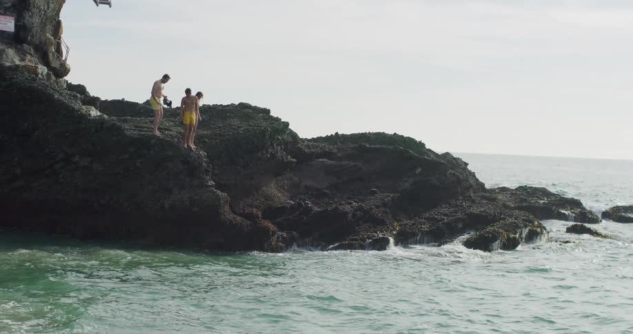 A group of people in swimming clothes stand over the ocean on a stone coastline