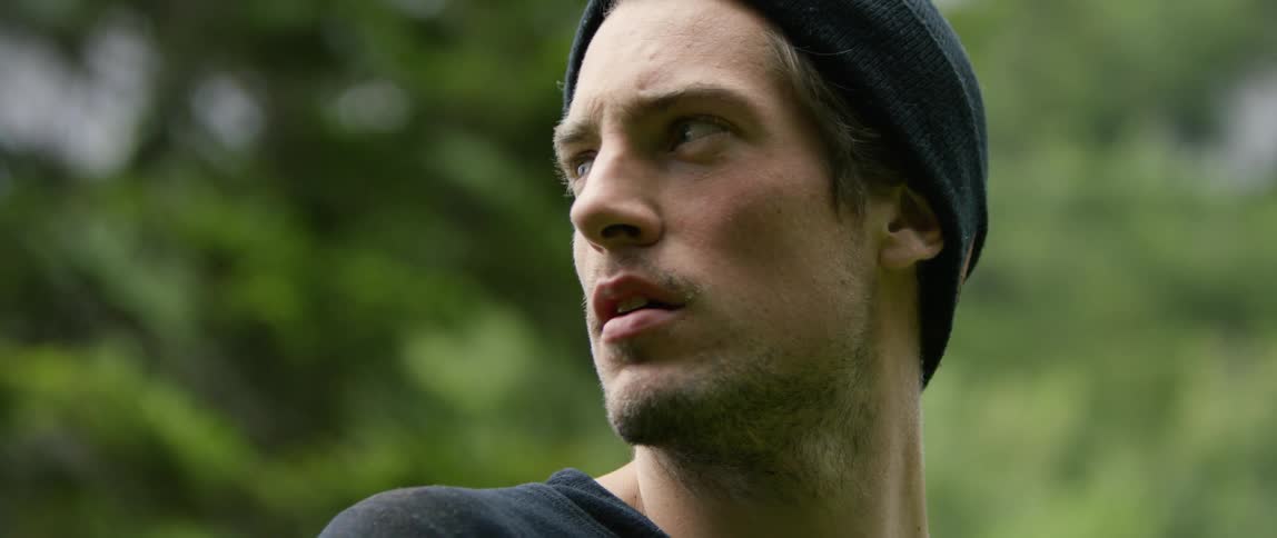 A man looks to his left and right as he stands outside in front of a large tree