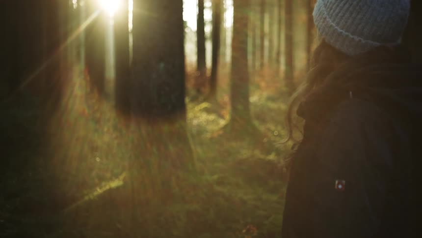 A woman is walking through a forest at dusk