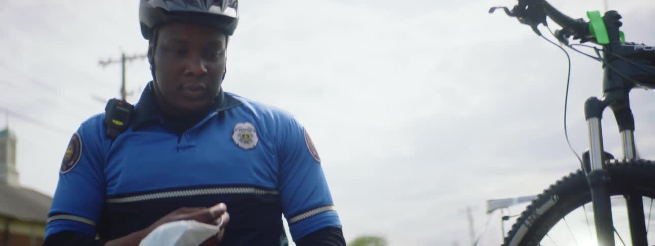 A police officer exits a police car and puts on his medical mask as he prepares to unload his bicycle from the cars rear