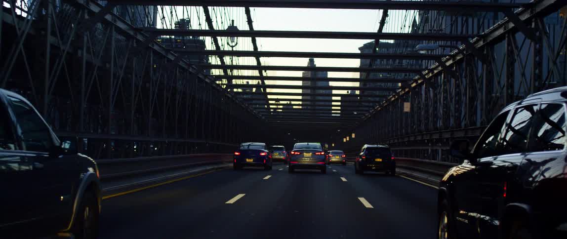 Traffic travels across a three lane bridge in a metropolis in the evening