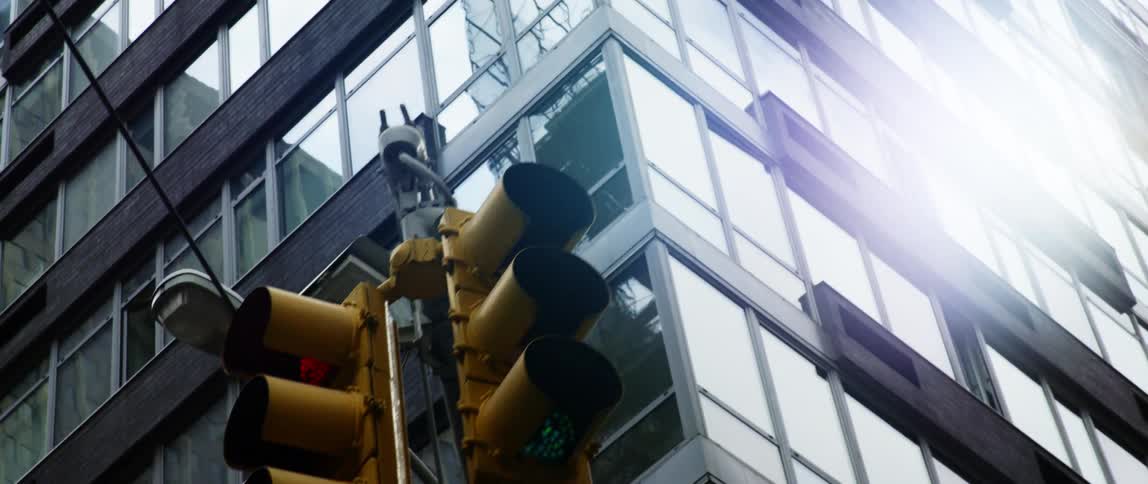 A window covered skyscraper and traffic light overhead in a city