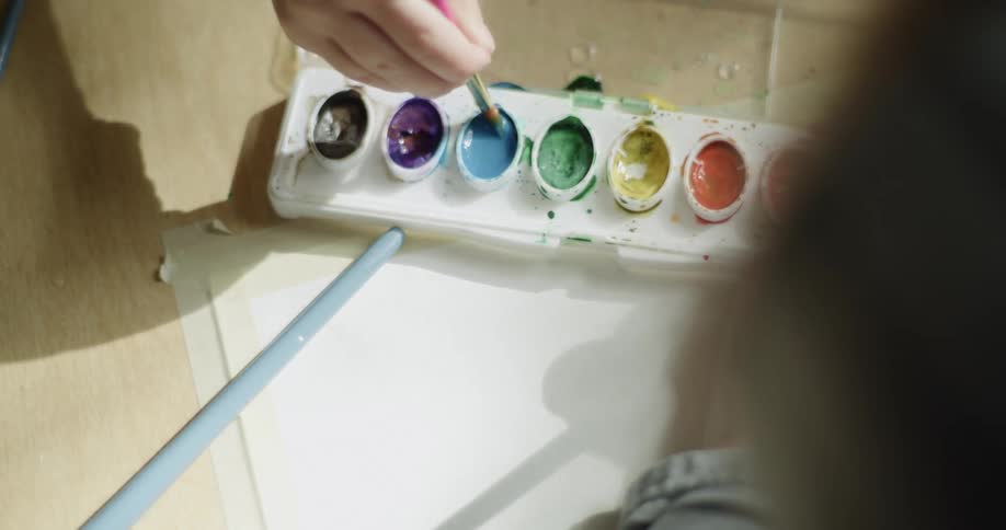 Small children using brushes to paint with colorful watercolors