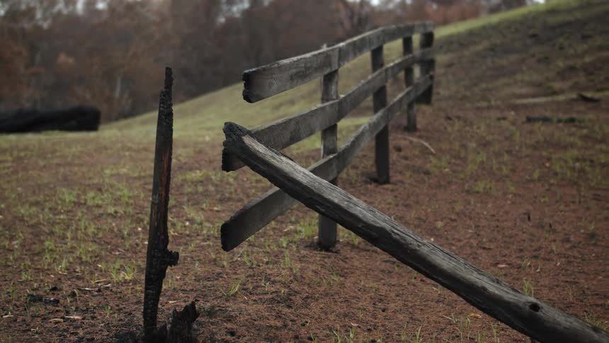 A broken wooden fence with a hill trees the sky and clouds in the background