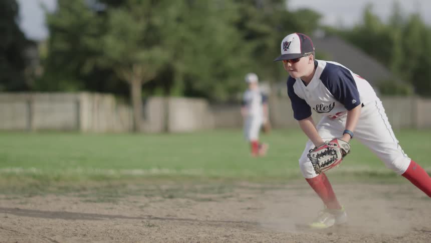 Boy picking up rolling baseball and tossing it to his teammate