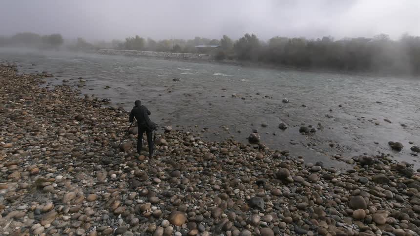 A man with a camera takes pictures of a mist covered river