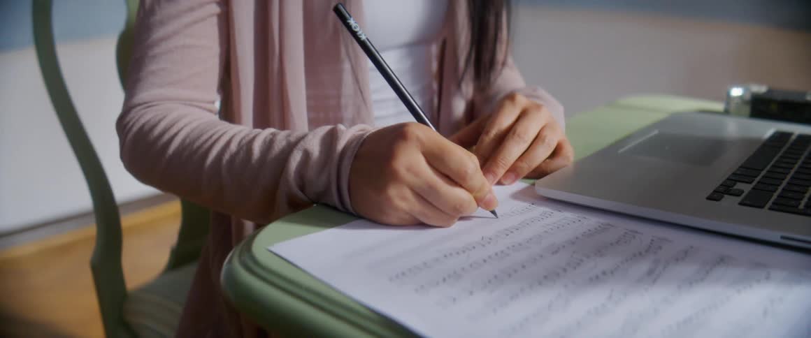A woman is writing next to her laptop
