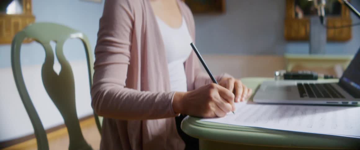 A woman is sitting at a desk and writing on a piece of paper