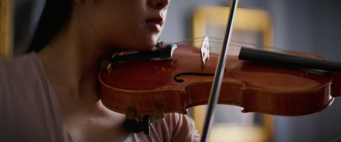 A woman playing a violin with a picture frame and a wall in the background