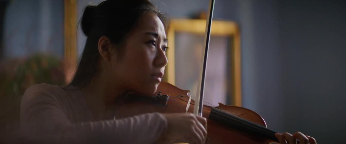 A young woman plays a violin indoors during the day