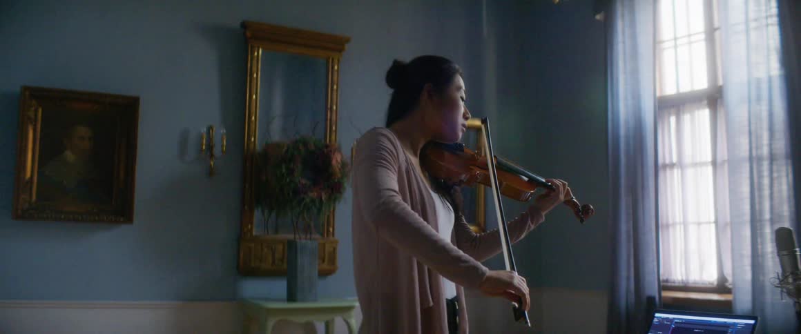 Standing woman plays violin in room near laptop and microphone
