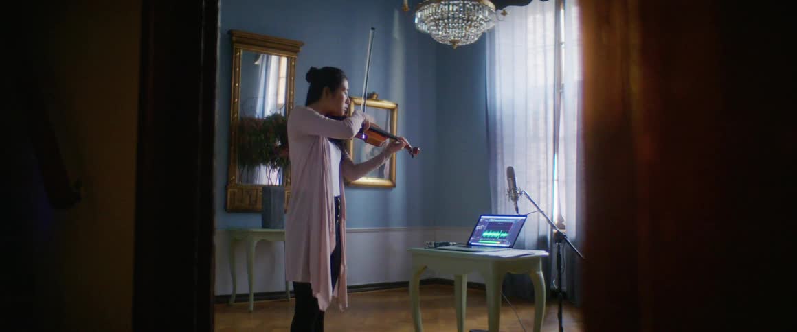 Woman plays violin standing near microphone and laptop