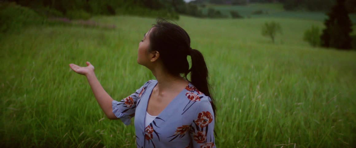 A woman smiles as she stands in a meadow and raises her arms up