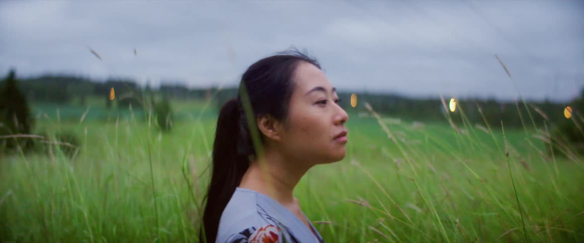 A woman is standing outdoors in a grassland area