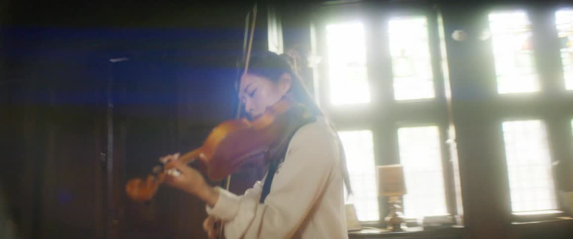 A young woman plays the violin in a large house during the day