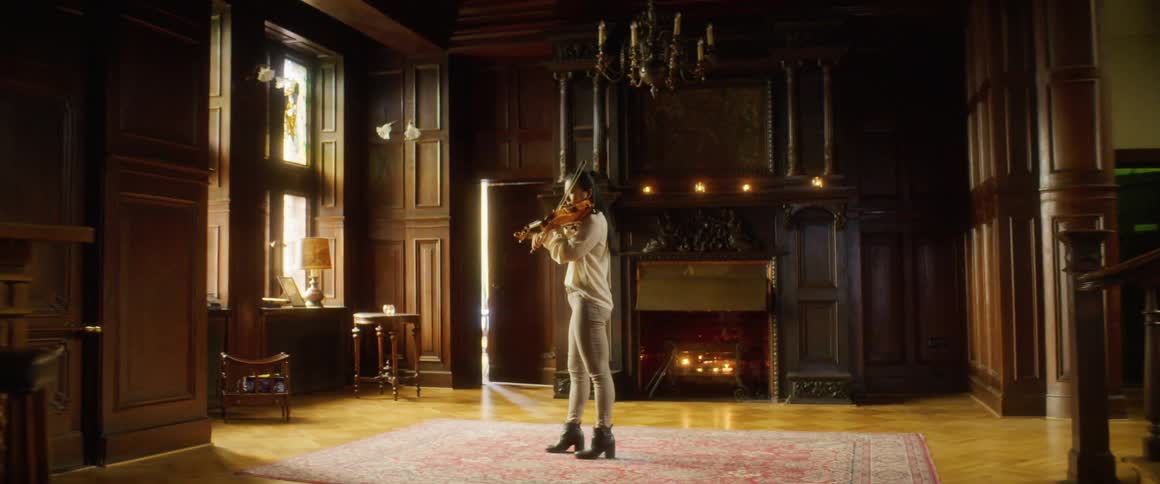 A woman plays the violin in a large open room with fireplace