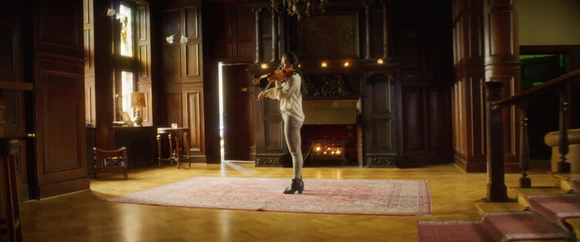A young asian woman plays the violin in front of a fireplace in a house during the day