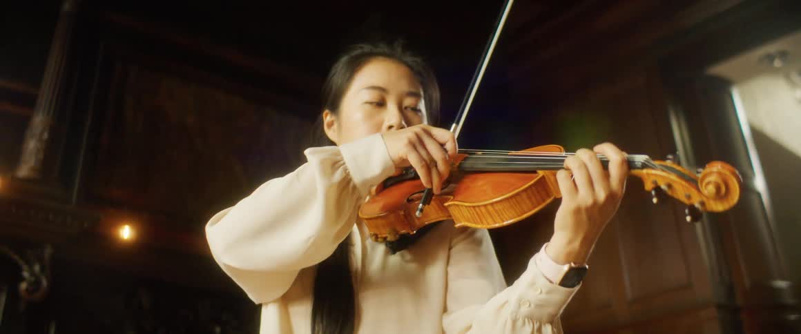 A young asian woman plays the violin in indoors during the day