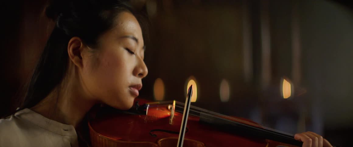 Asian female violinist with a white blouse plays a violin in a large room