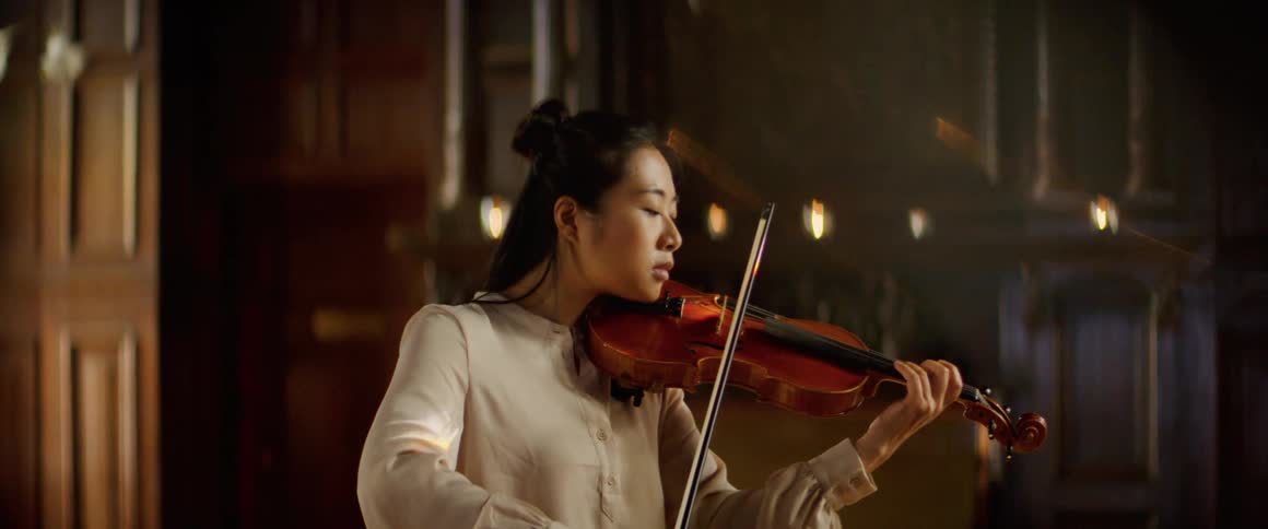 Woman plays violin in large dimly lit room
