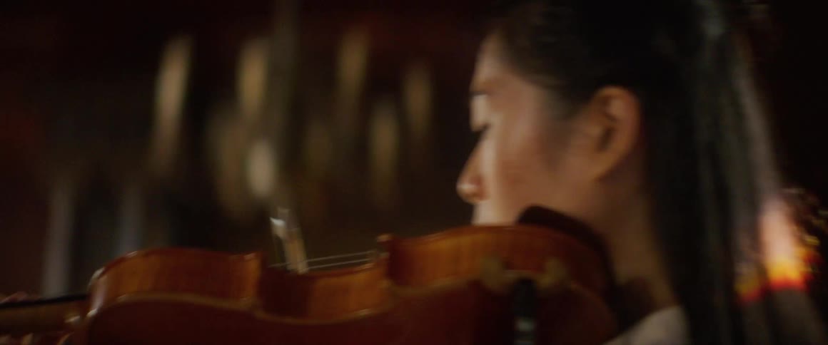A woman plays the violin while standing in front of the hearth in a building during the day