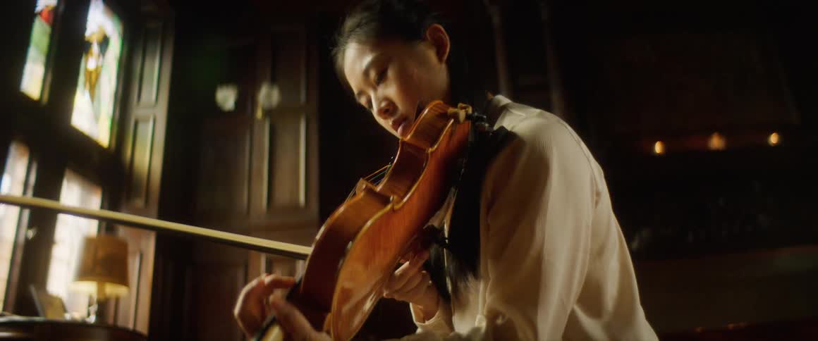 A young asian woman adjusts her violin on her shoulder before beginning to play