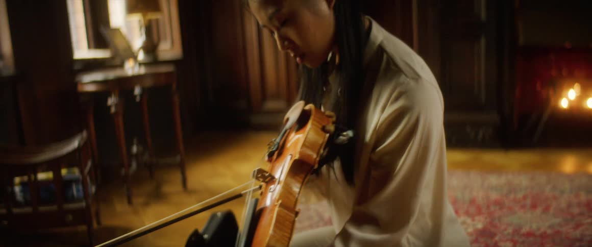 A young woman kneels on a rig at home and looks at her violin