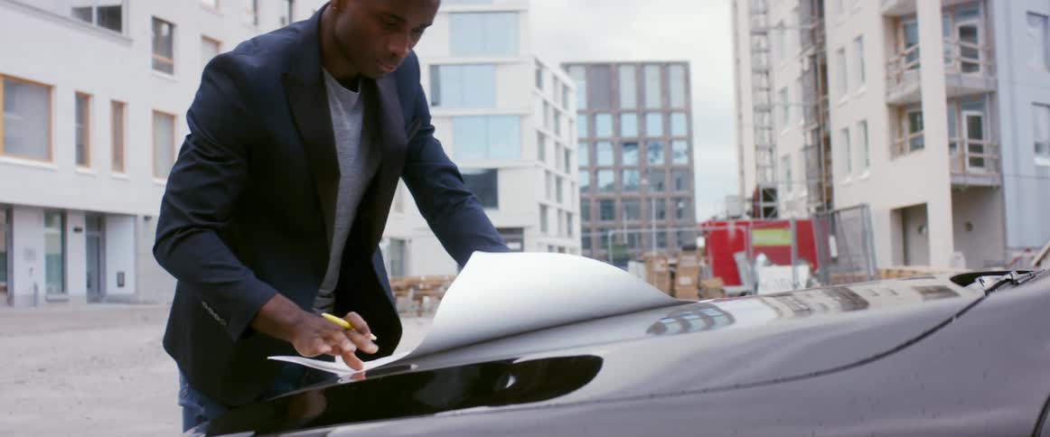 Man examines plan on car hood near building construction site