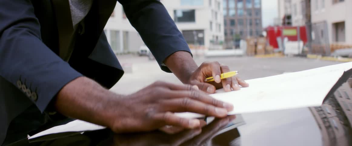 A man at a construction site looks at paperwork on the hood of his car