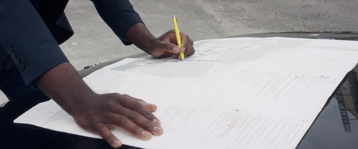 Manleans over reflective hood of car parked in parking lot writing on large paper