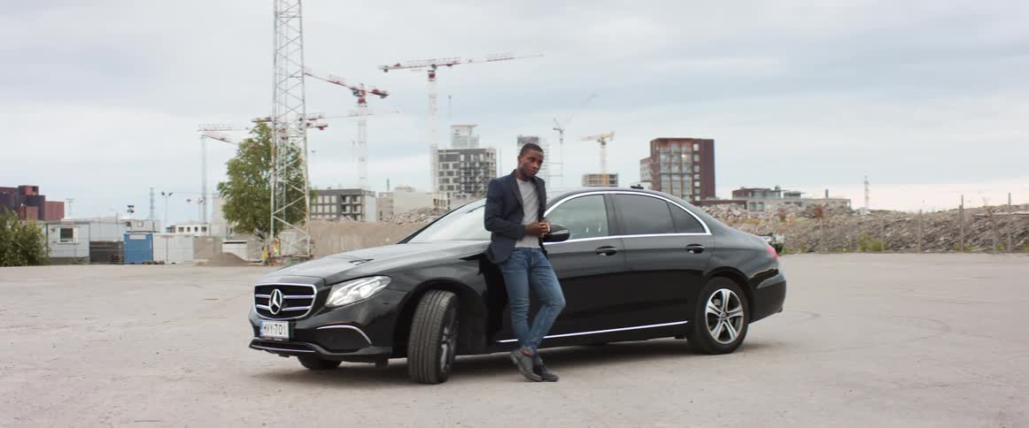A leather clad man rests against a black sports car