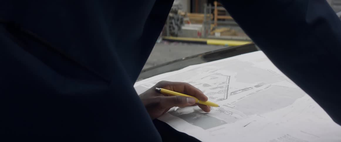 A man looks at blueprints on the hood of a car at a construction site