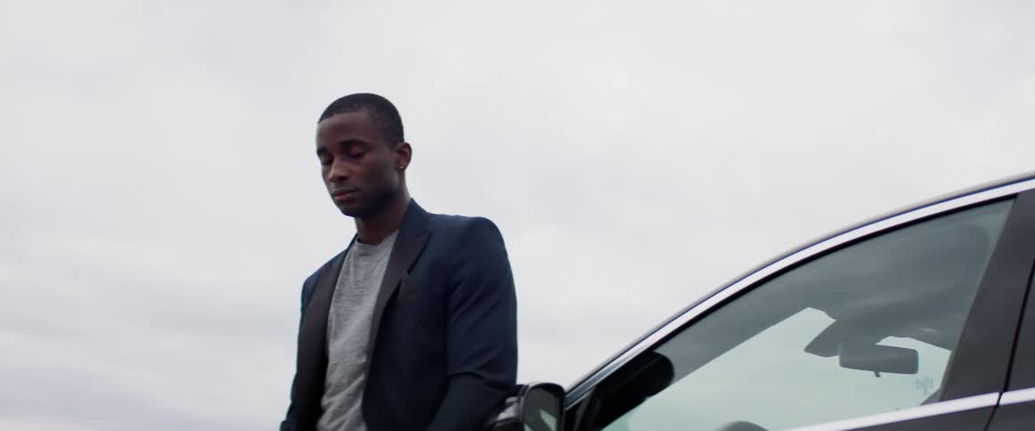 A young man leans against his car outside