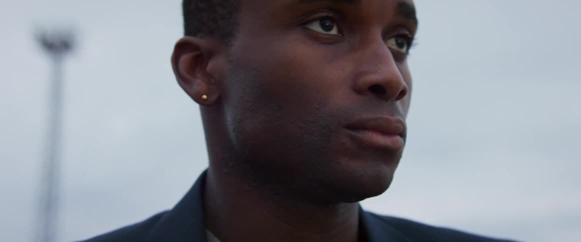 A man with a somber expression on his face stands outdoors during the day