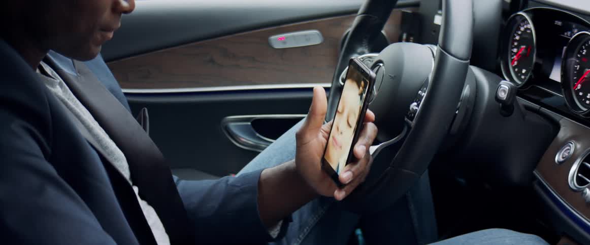 A man video chats with a child with his smartphone while sitting in the drivers seat of a vehicle during the day